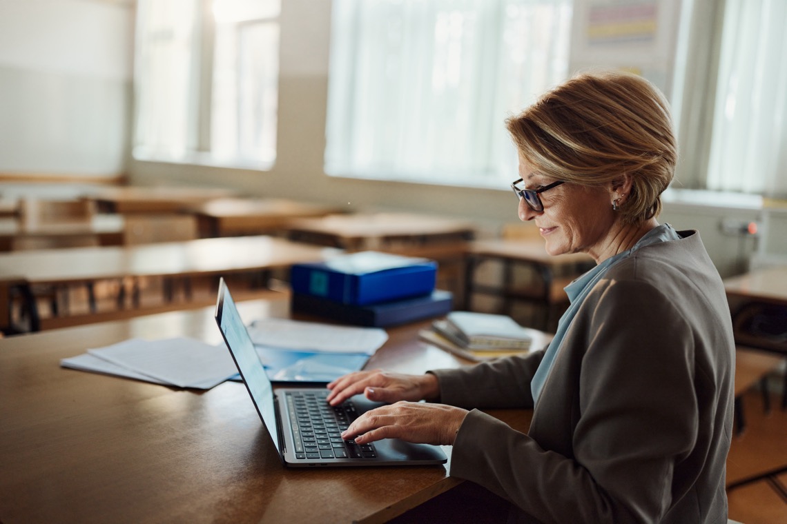teacher working on laptop in an empty classroom